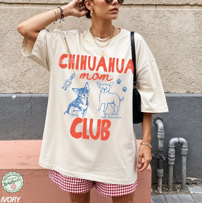 Person wearing a t-shirt with 'Chihuahua mom club' design against a wall.
