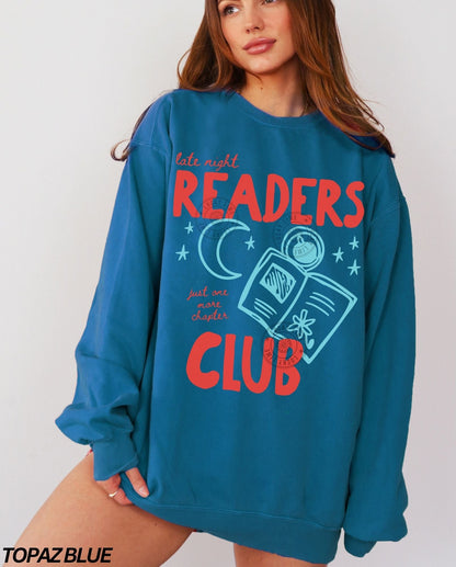 Person wearing a topaz blue sweatshirt with 'late night readers club' text and graphics on a plain background