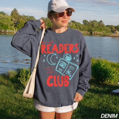 Person wearing a denim sweatshirt with 'late night Readers Club' text by a lake.