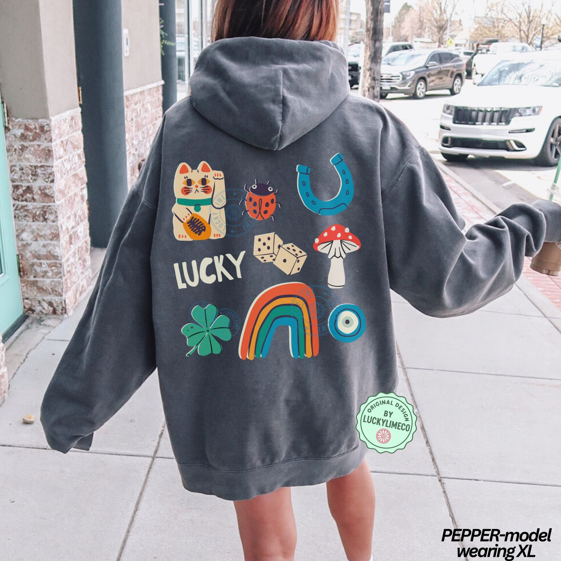 Person wearing a gray hoodie with colorful lucky icon designs on the back, standing on a sidewalk.