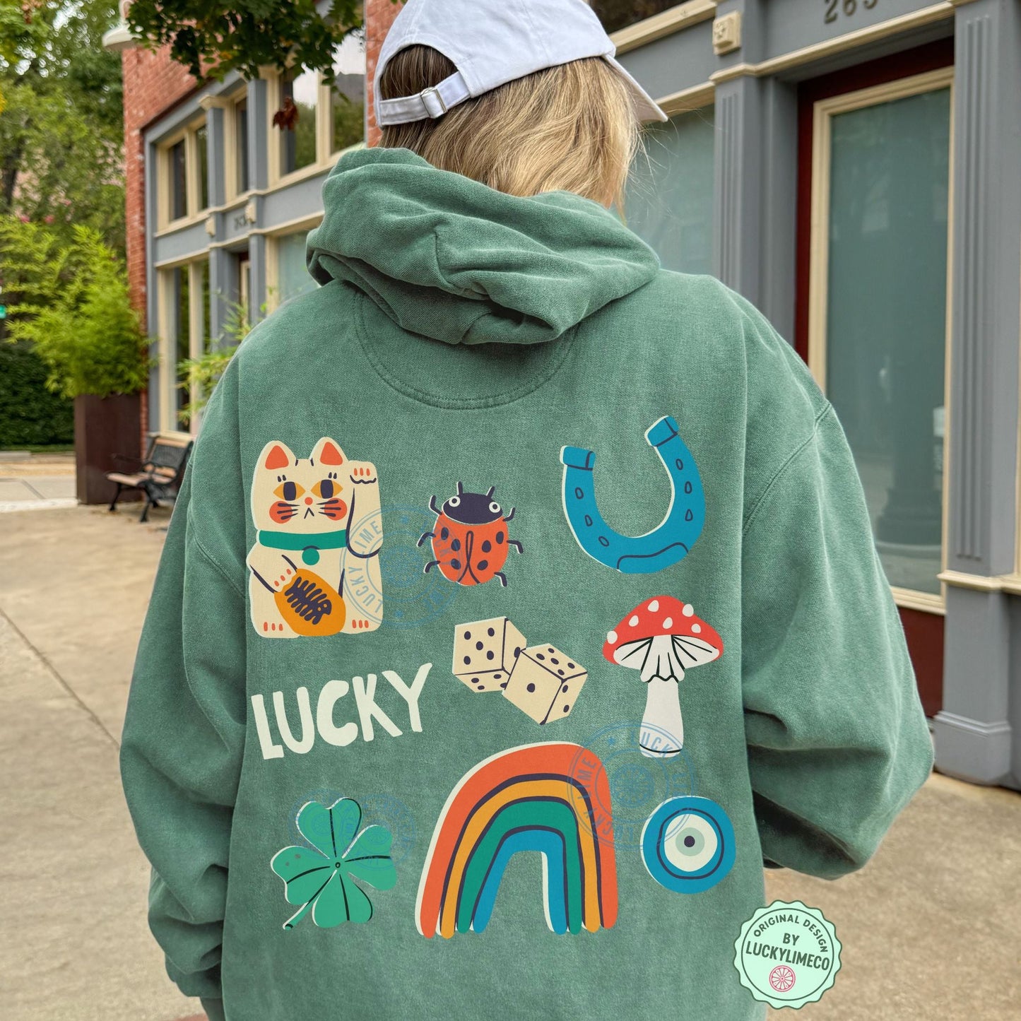 Person wearing a green hoodie with colorful lucky icon designs and text, standing on a sidewalk.