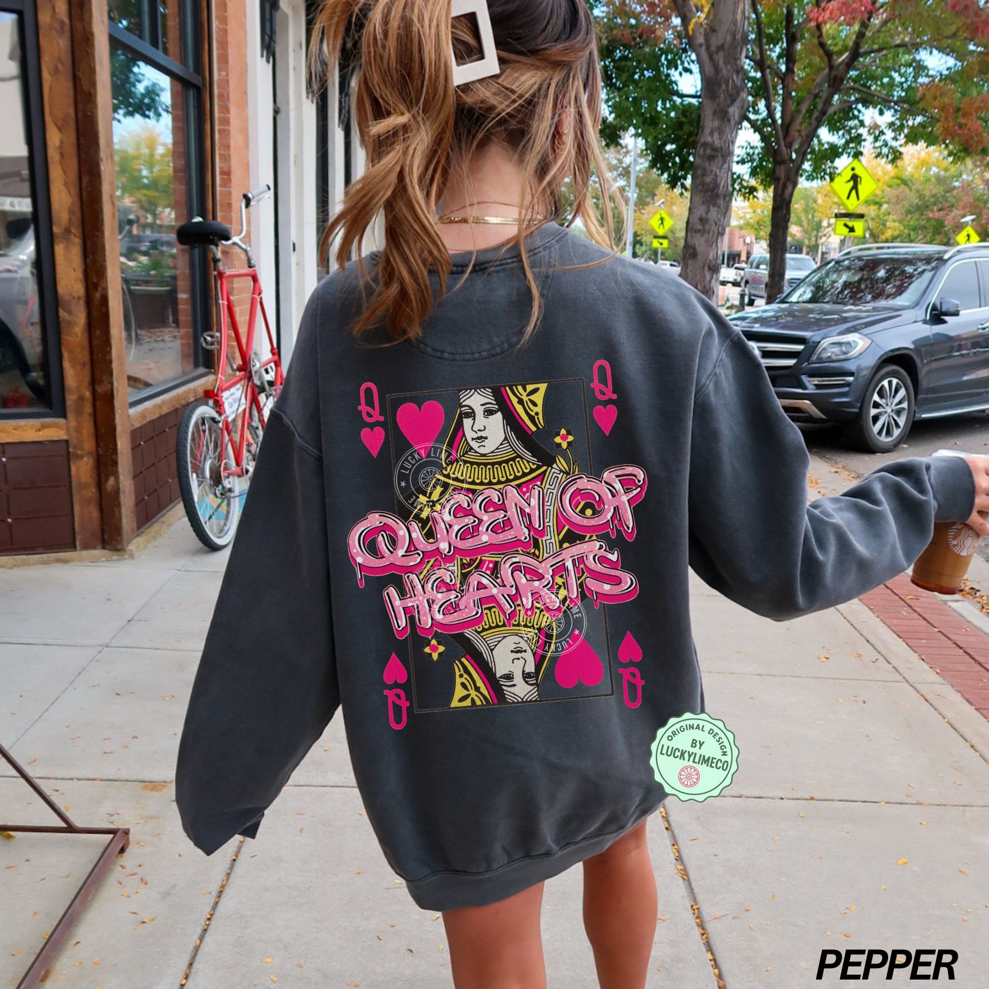 Person wearing a pepper colored sweatshirt with 'Queen of Hearts' design on a sidewalk.