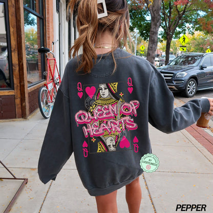 Person wearing a pepper colored sweatshirt with 'Queen of Hearts' design on a sidewalk.