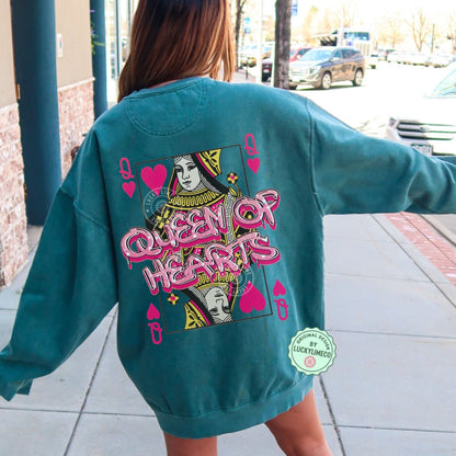 Person wearing a teal sweatshirt with 'Queen of Hearts' design on the back, standing on a sidewalk.