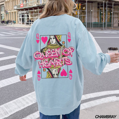 Person wearing a light blue sweatshirt with 'Queen of Hearts' design on a city street.