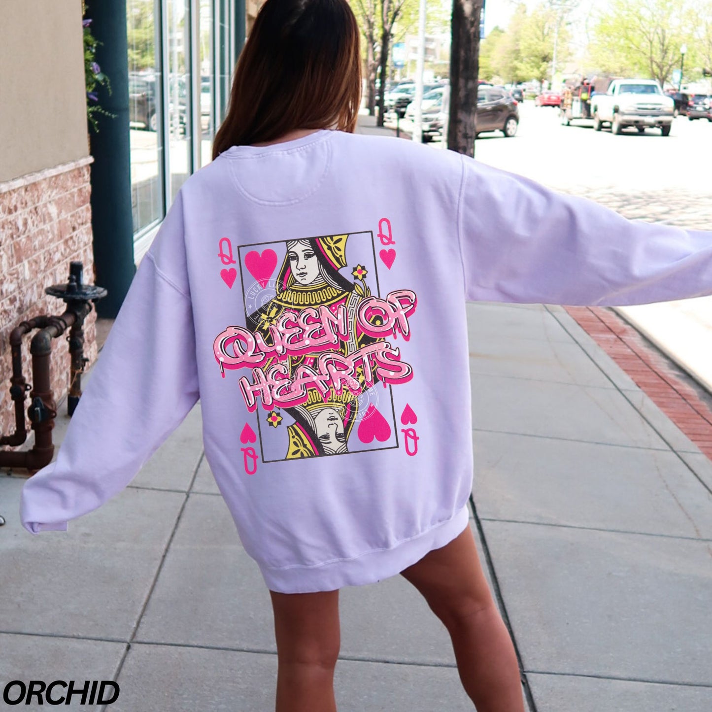 Person wearing a light purple sweatshirt with a g
Queen of Hearts graphic on the back, standing on a sidewalk.