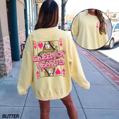 Person wearing a yellow sweatshirt with 'Queen of Hearts' design on a sidewalk.
