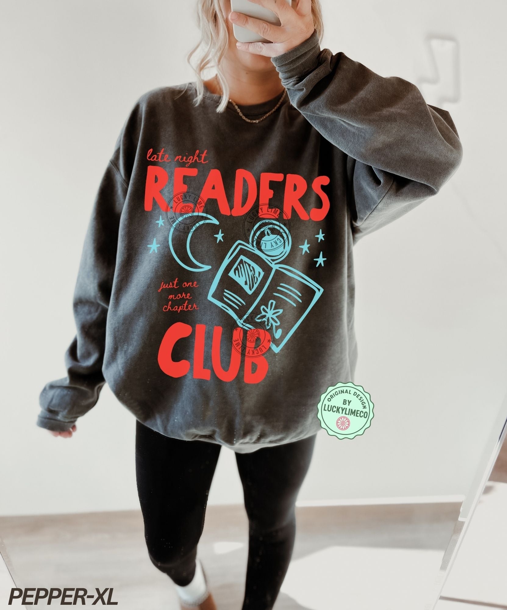 Person wearing a gray sweatshirt with 'Late Night Readers Club' design, holding a phone.