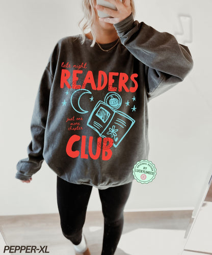 Person wearing a gray sweatshirt with 'Late Night Readers Club' design, holding a phone.