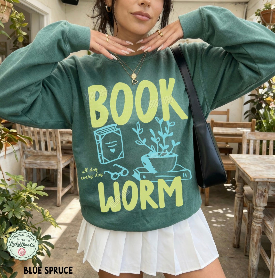 Person wearing a green sweatshirt with 'BOOK WORM' text and graphics in an outdoor setting.