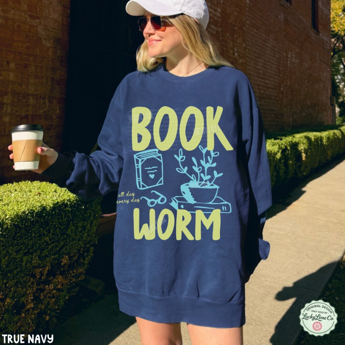 Person wearing a navy sweatshirt with 'BOOK WORM' text, holding a coffee cup outdoors.