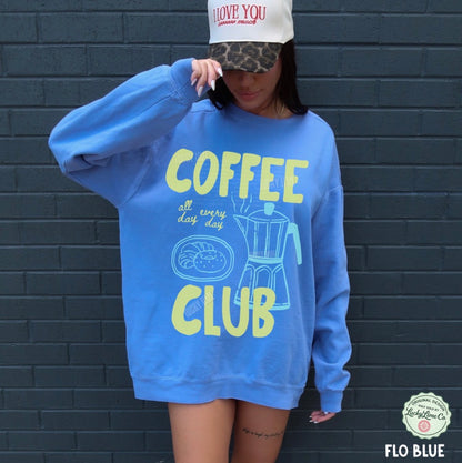 Person wearing a blue 'Coffee Club' sweatshirt against a dark brick wall.