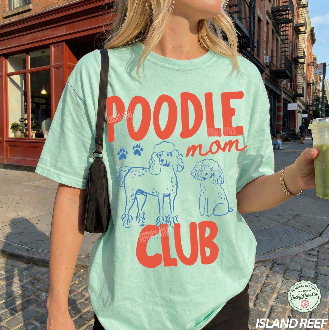 Person wearing a light green t-shirt with 'Poodle Man Club' design on a city street.