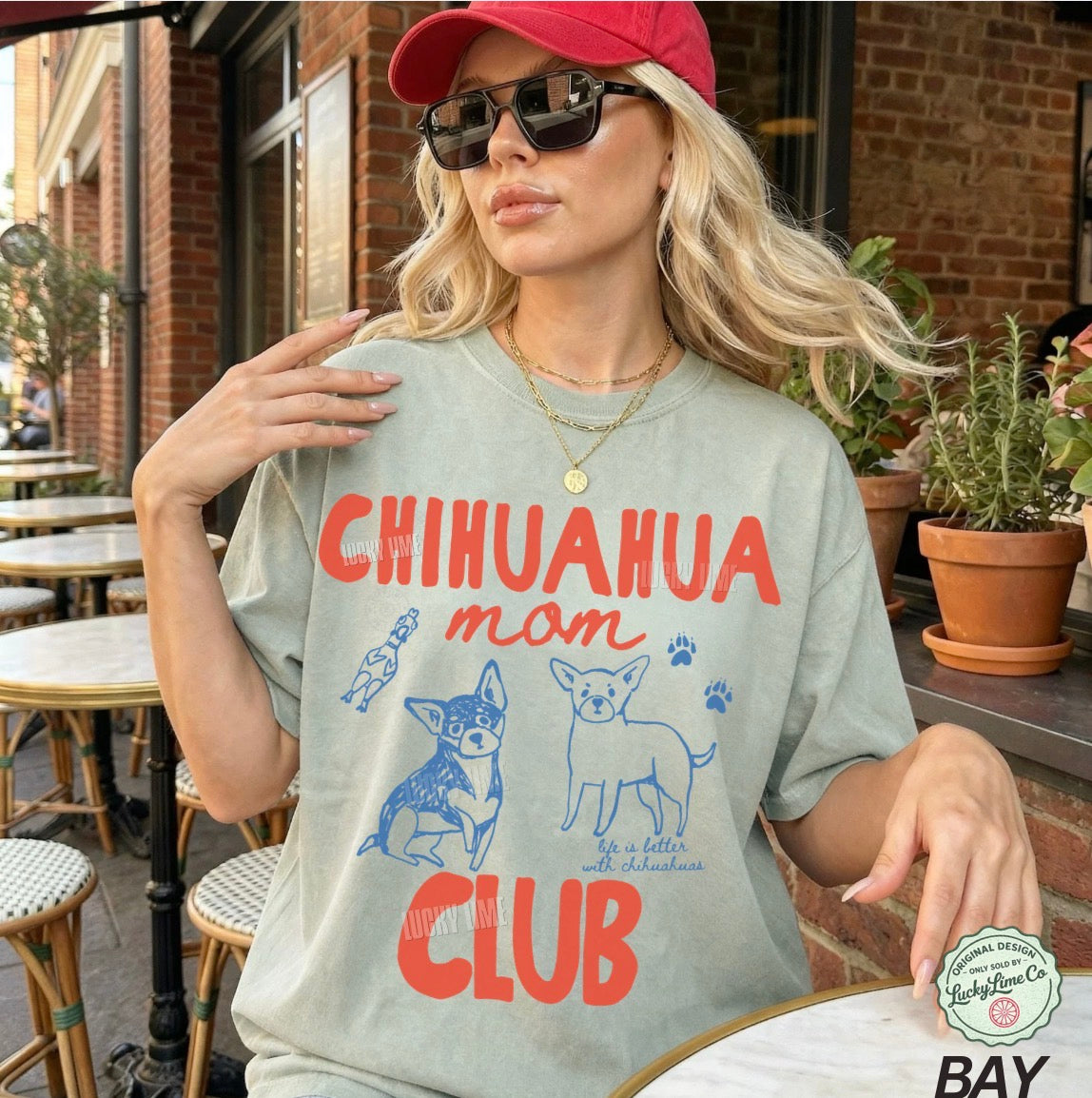 Woman wearing a t-shirt with 'Chihuahua mom club' text and graphics outdoors.