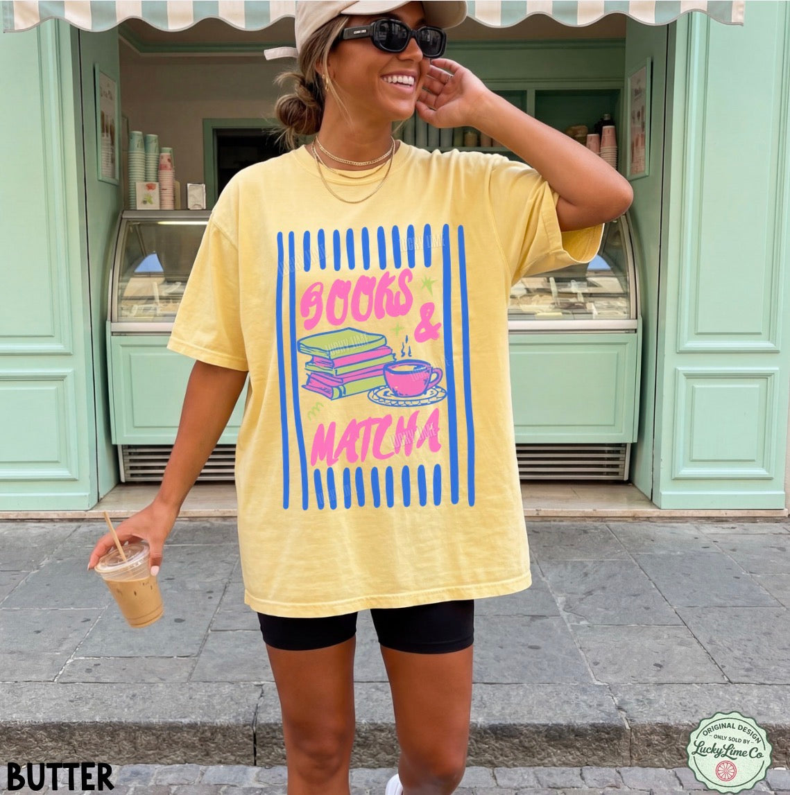 Woman wearing a yellow t-shirt with graphic design and text, standing in front of a light green building.