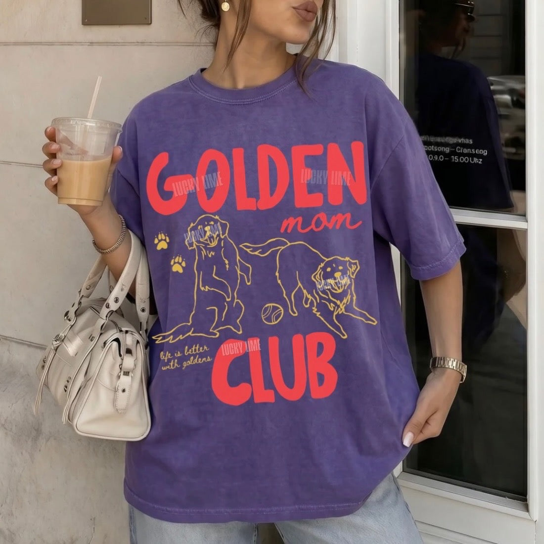 A woman wearing a purple oversized graphic T-shirt with red and yellow text reading 'GOLDEN man CLUB' and dog illustrations, holding a drink and a white handbag in an outdoor storefront setting.