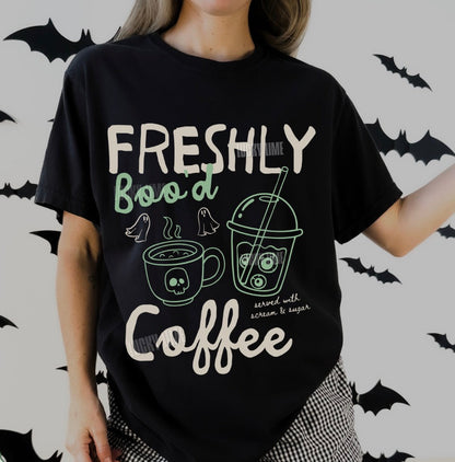 Person wearing a black t-shirt with 'Freshly Boo'd Coffee' text and graphics on a Halloween-themed background.