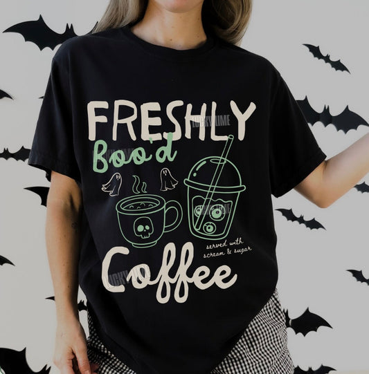 Person wearing a black t-shirt with 'Freshly Boo'd Coffee' text and graphics on a Halloween-themed background.
