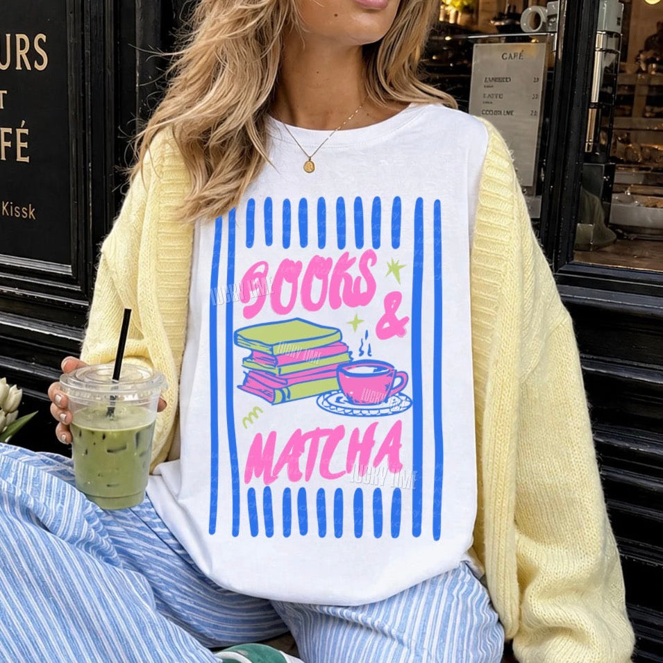 Person wearing a white sweatshirt with 'Books & Matcha' design, sitting in front of a cafe.