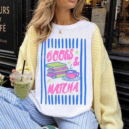 Person wearing a white sweatshirt with 'Books & Matcha' design, sitting in front of a cafe.