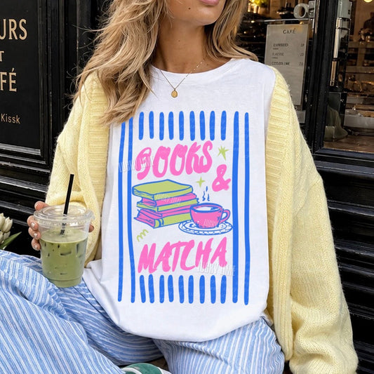 Person wearing a white sweatshirt with 'Books & Matcha' design, sitting in front of a cafe.
