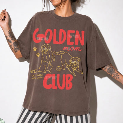 A person wearing an oversized brown graphic T-shirt with red and yellow text reading 'Golden Moon Club' and a yellow dog illustration, paired with black-and-white striped pants against a plain light background.