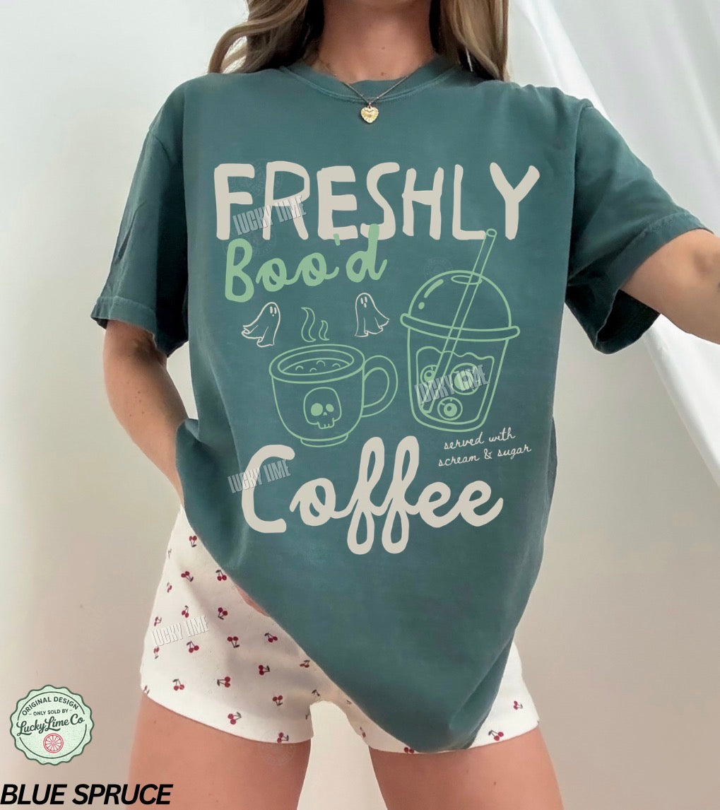 Person wearing a teal t-shirt with 'Freshly Bood Coffee' text and graphics on a white background