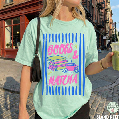 Person wearing a light green t-shirt with 'Books & Matcha' design, holding a drink on a city street.