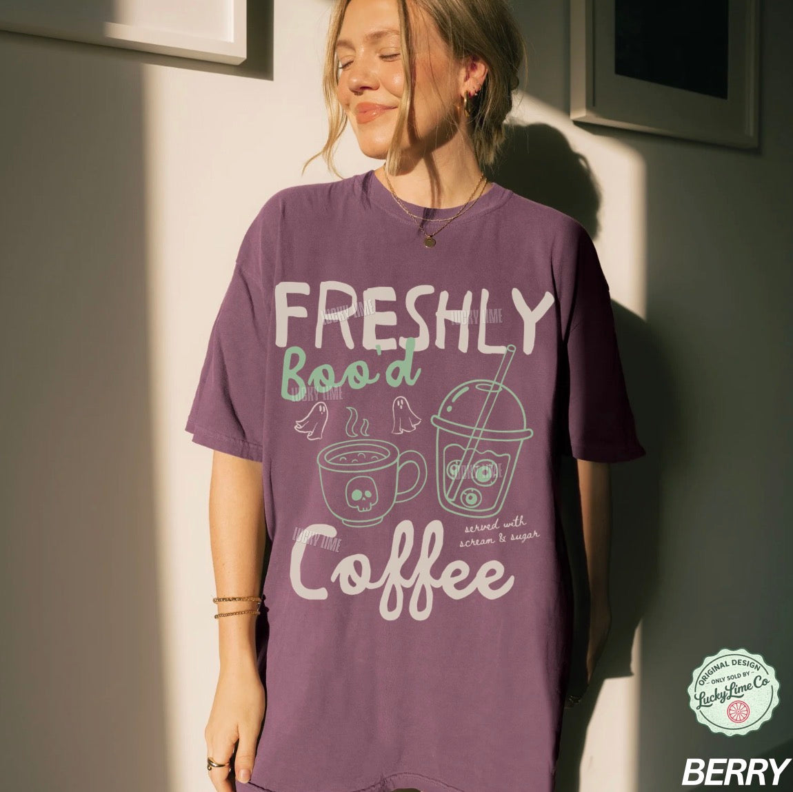 Person wearing a purple t-shirt with 'Freshly Bod Coffee' design, standing against a neutral wall.