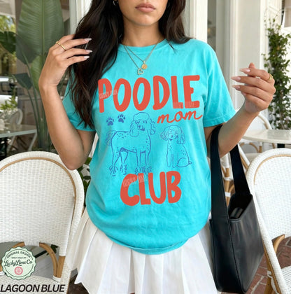 Woman wearing a turquoise t-shirt with 'Poodle Mom Club' text and dog graphics outdoors.