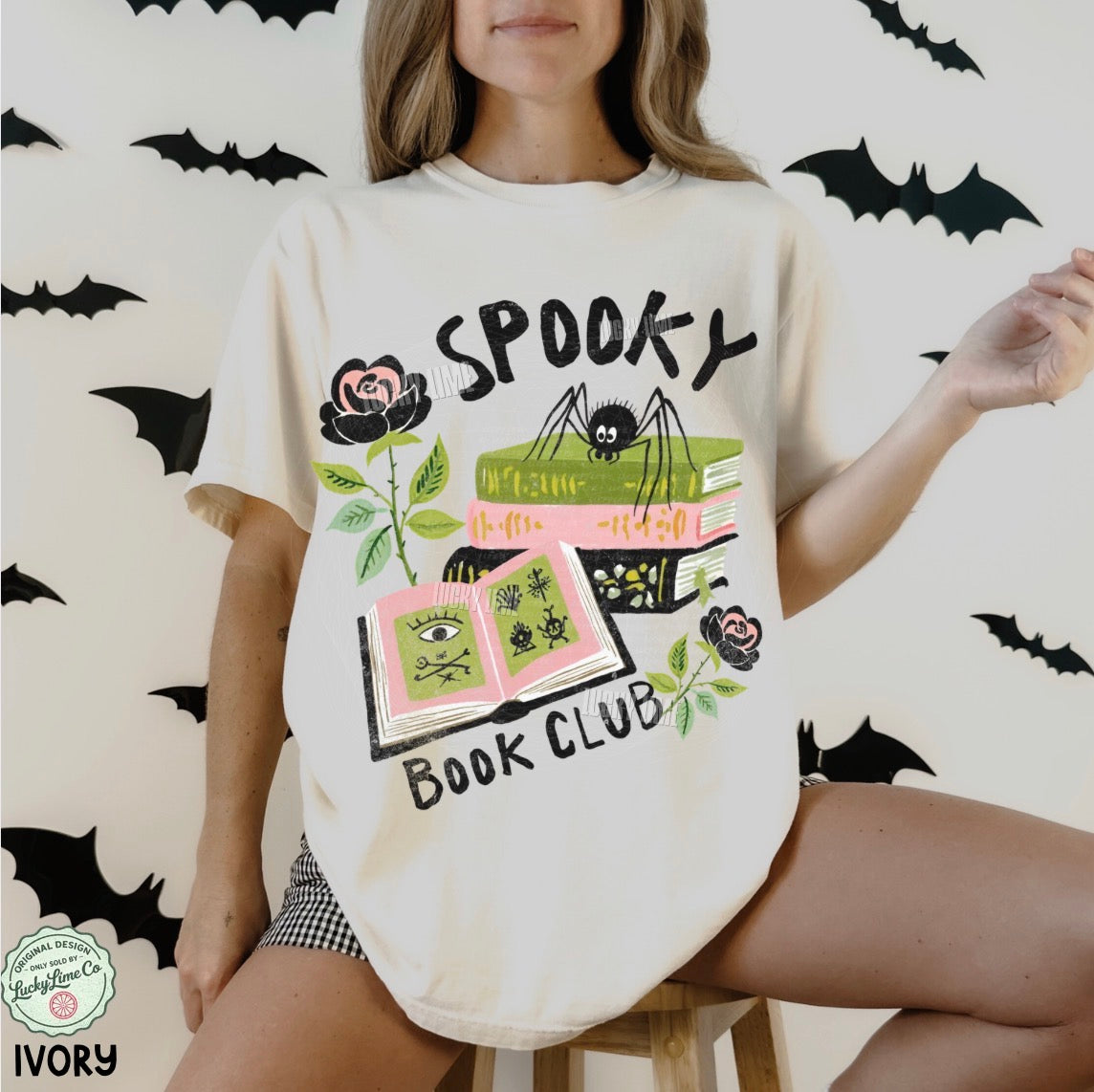 Person wearing a 'Spooky Book Club' t-shirt with Halloween-themed graphics on a white background with bats.