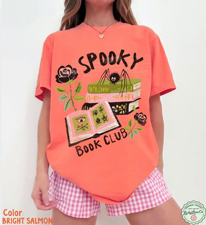Person wearing a bright salmon t-shirt with 'Spooky Book Club' design and pink checkered shorts.