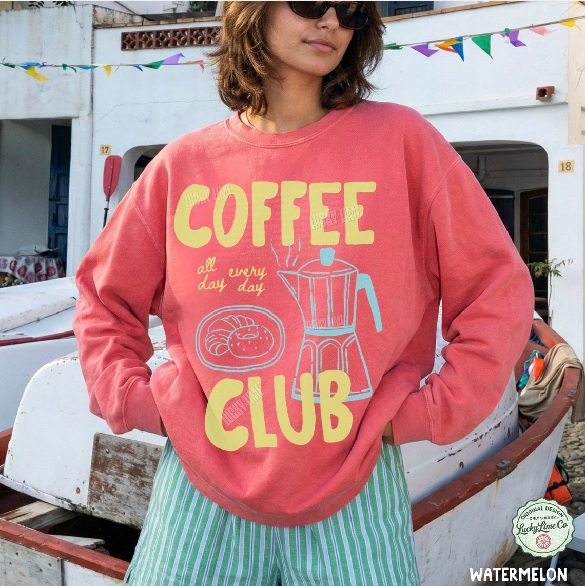 Person wearing a pink sweatshirt with 'Coffee Club' text and graphics, standing outdoors.