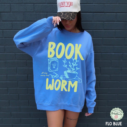 Person wearing a blue sweatshirt with 'BOOK WORM' text against a dark brick wall.