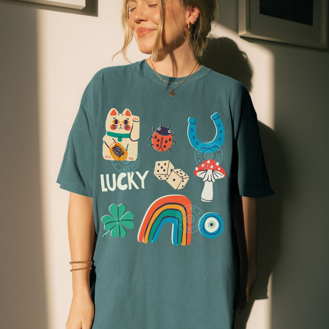 Person wearing a teal t-shirt with colorful lucky charms graphics and text, standing against a light-colored wall.