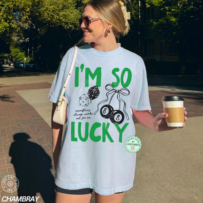 Woman wearing a light blue t-shirt with 'I'm so lucky' text and graphics, holding a coffee cup outdoors.