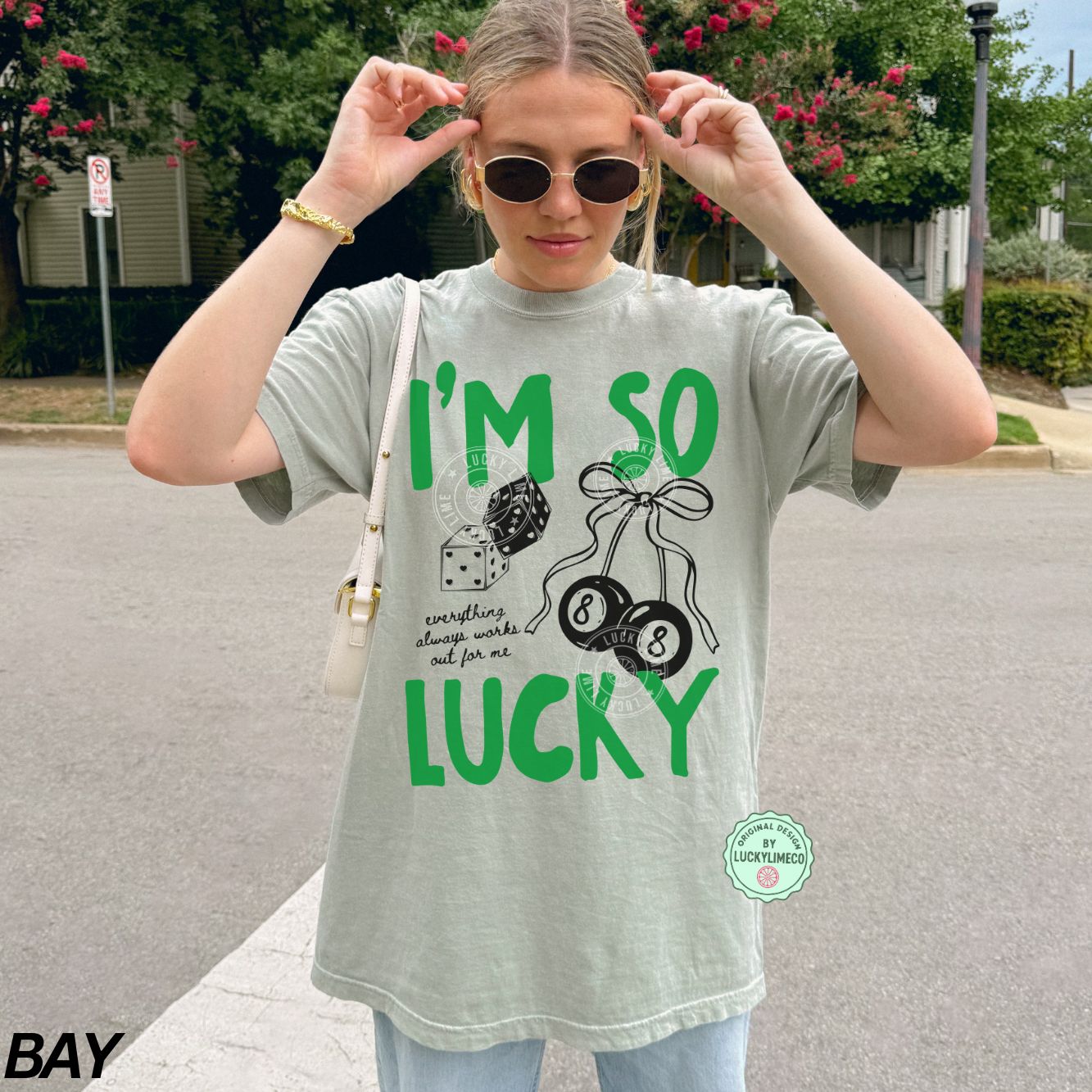 Woman wearing a bay comfort colors t-shirt with 'I'm so lucky' text and graphics outdoors.