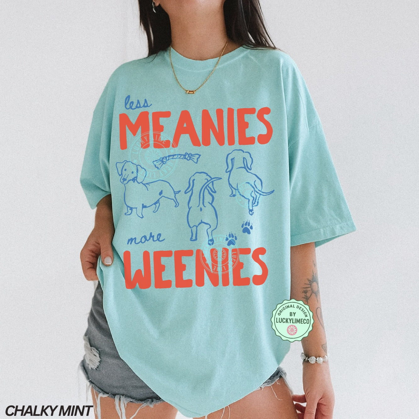 Person wearing a light blue t-shirt with 'less MEANIES more WEENIES' text and graphics on a plain background.
