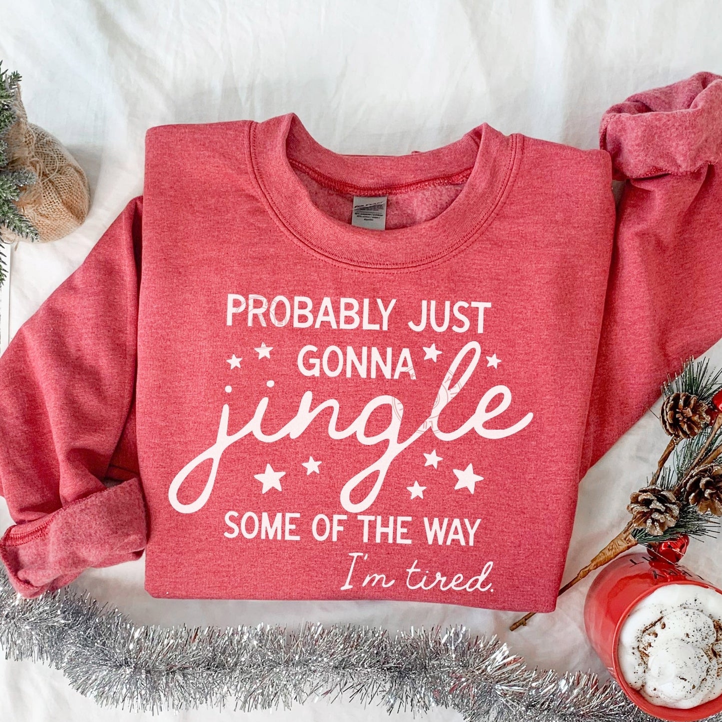 Red sweatshirt with Christmas-themed text on a white surface with holiday decorations.