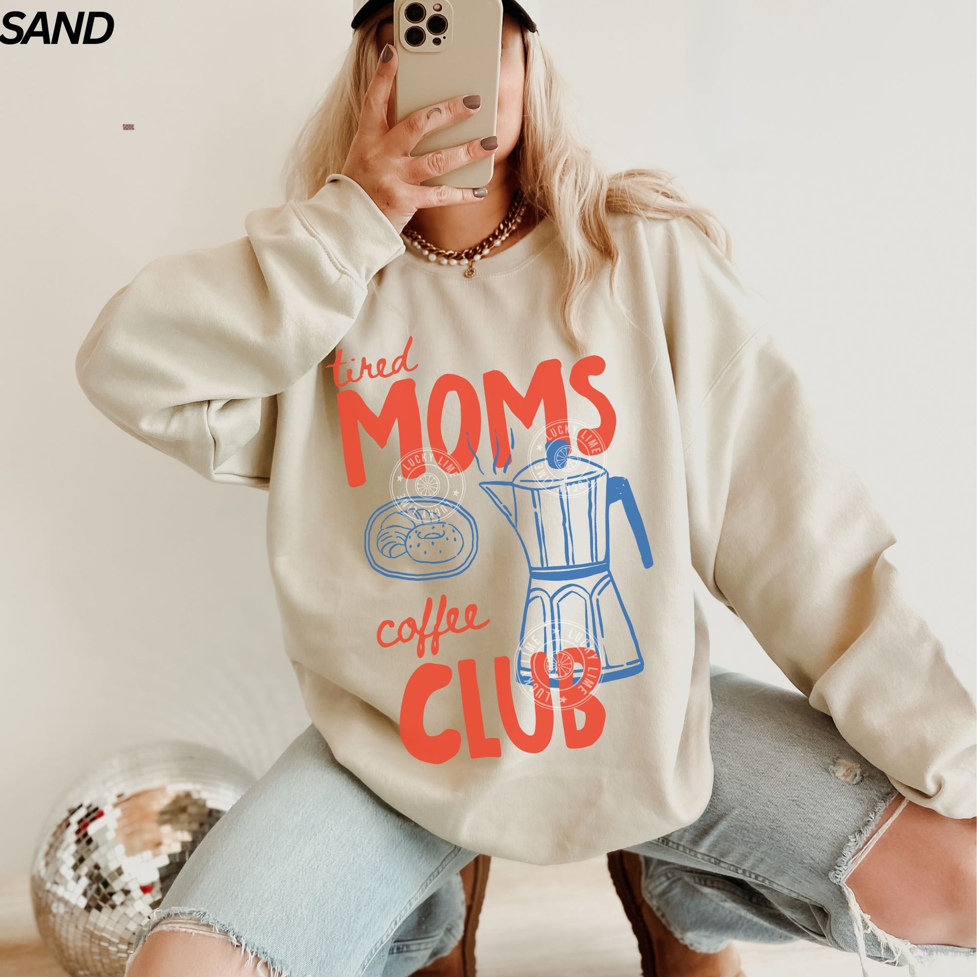 Person wearing a sweatshirt with 'tired Moms Coffee Club' text and graphic.