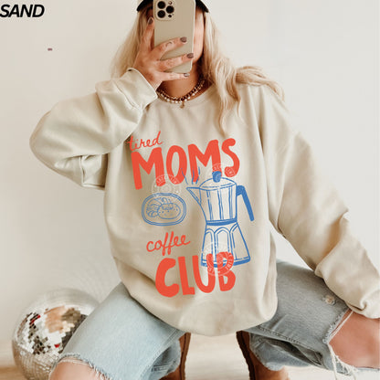 Person wearing a sweatshirt with 'tired Moms Coffee Club' text and graphic.