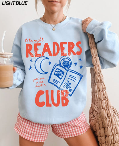 Person wearing a light blue sweatshirt with 'Late Night Readers Club' text and red shorts, holding a bag and drink.
