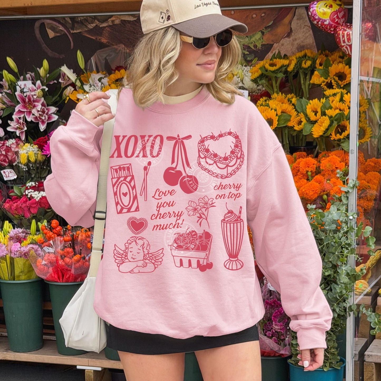 Woman wearing a light pink sweatshirt with red Valentine graphics in front of a flower shop.