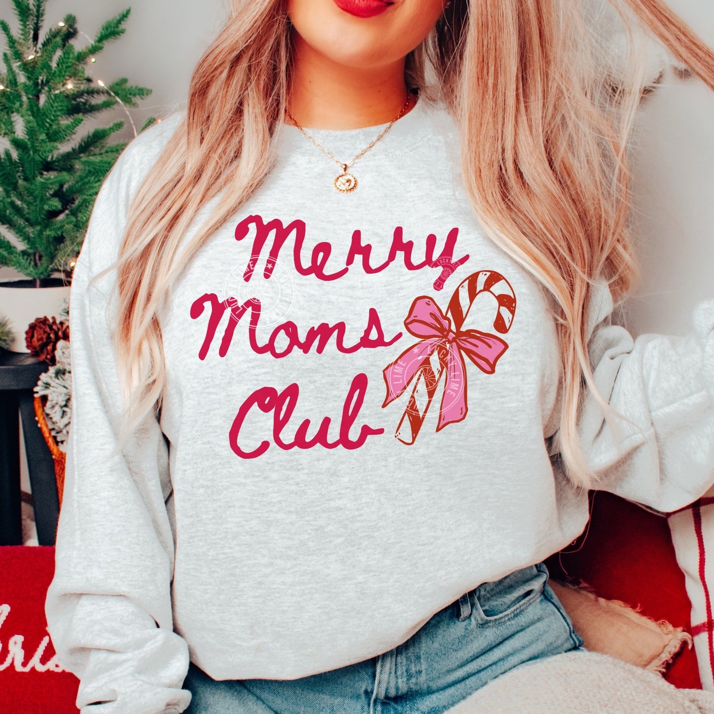 Person wearing a white sweatshirt with 'Merry Moms Club' text and candy cane design, sitting in a festive setting.