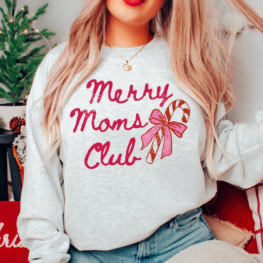 Person wearing a white sweatshirt with 'Merry Moms Club' text and candy cane design, sitting in a festive setting.