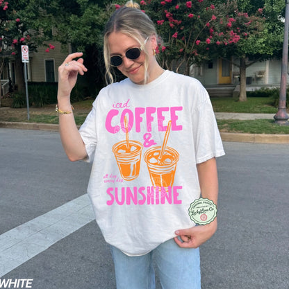 Person wearing a white t-shirt with 'iced coffee & sunshine' design outdoors.