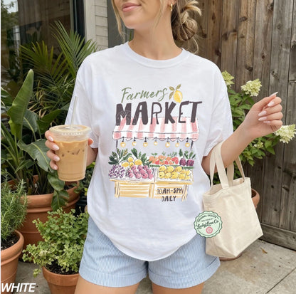 Person wearing a 'Farmers Market' t-shirt holding a drink and a bag, standing outdoors with plants.
