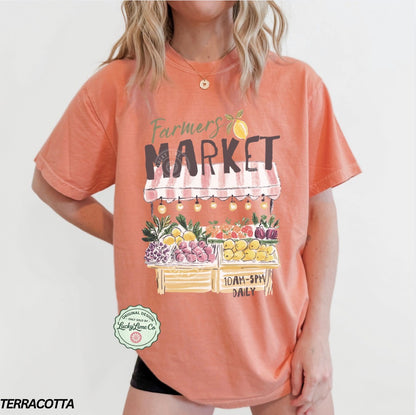 Person wearing a terracotta-colored t-shirt with 'Farmers Market' graphic and text.