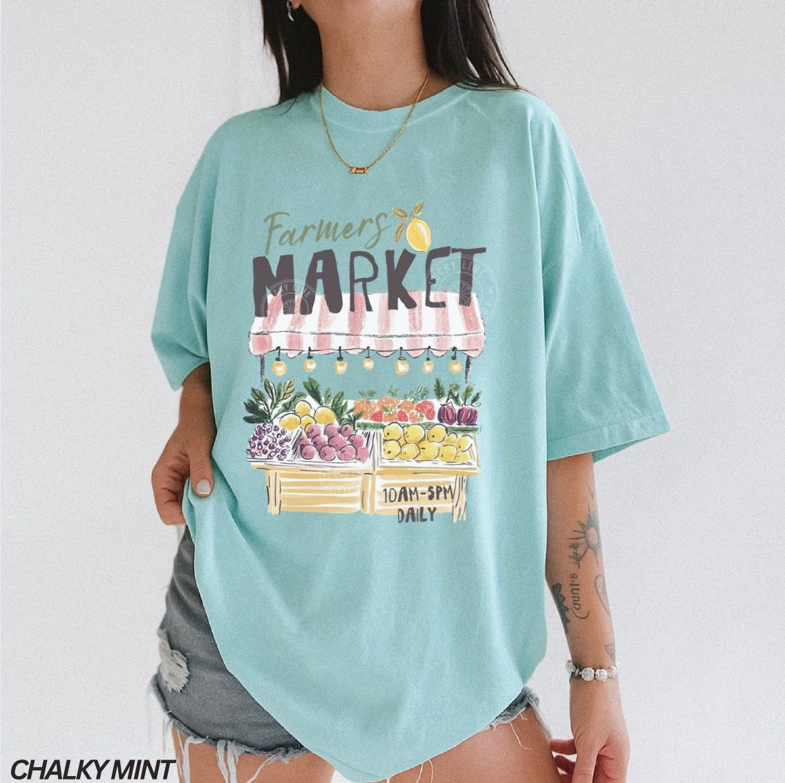 Light blue t-shirt with 'Farmers Market' graphic worn by a person on a plain background