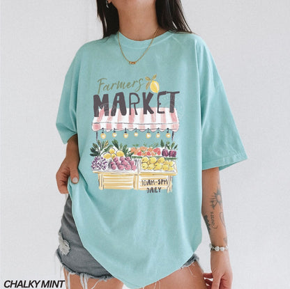 Light blue t-shirt with 'Farmers Market' graphic worn by a person on a plain background